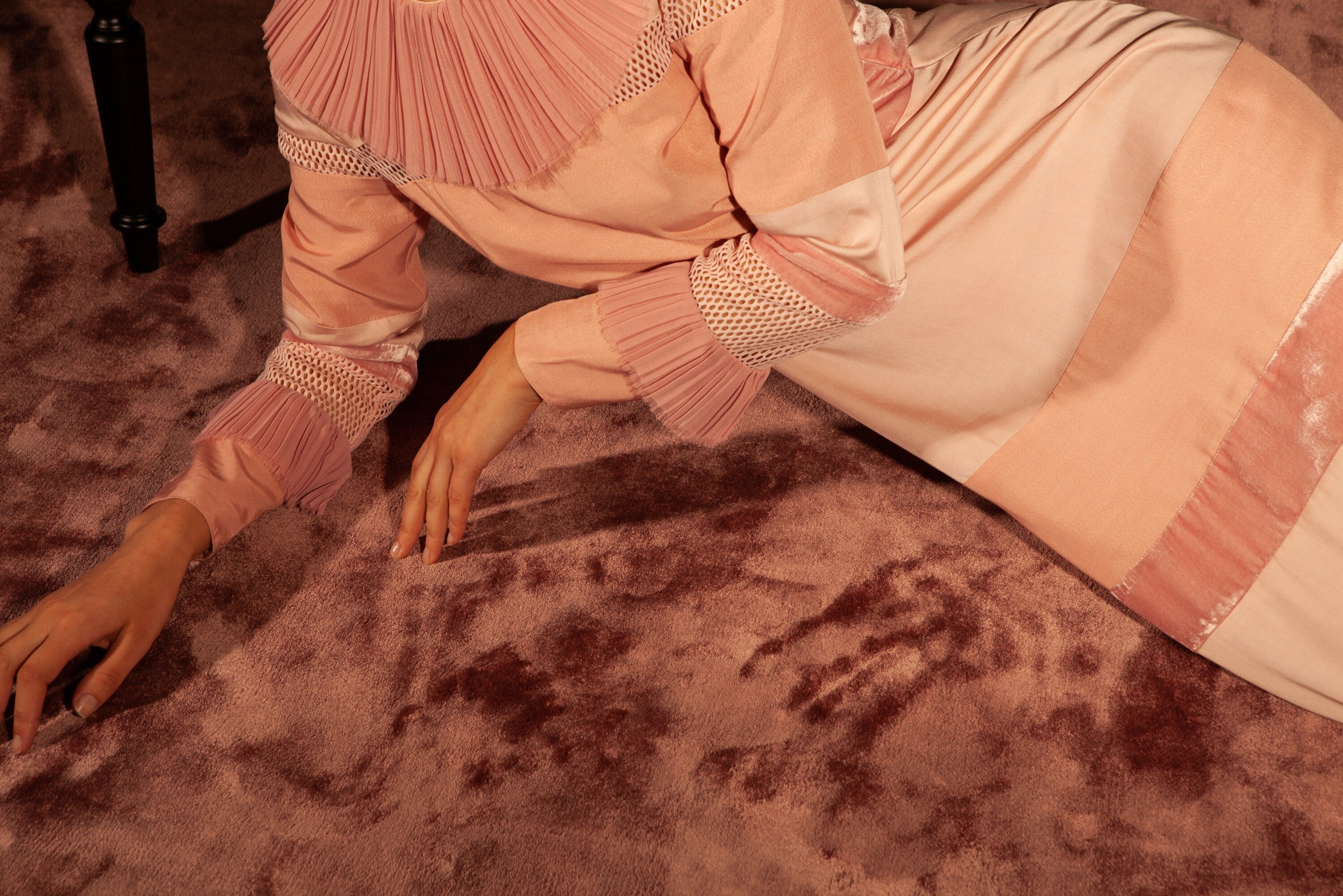 The model lies on her side on a luxurious pink carpet. The dress has panels of slightly shiny bamboo silk, silk velvet, mat silk twill, sheer sportswear mesh and sheer chiffon. All are a peachy shade of pink but in slightly different tones.