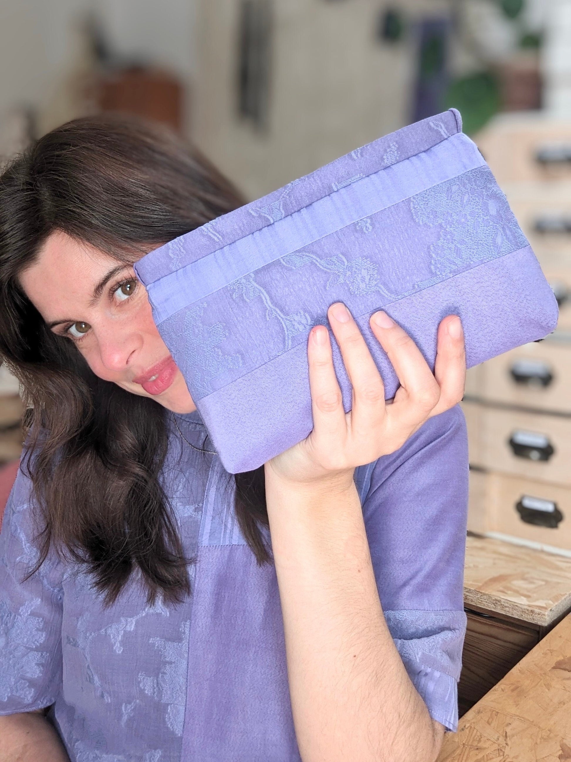 This picture shows me holding the makeup bag. I have white skin and brown hair. I am smiling and hold the makeup bag close to the camera slightly in front of my face. I am wearing a t shirt dress which is made from the exact same fabrics as the purse